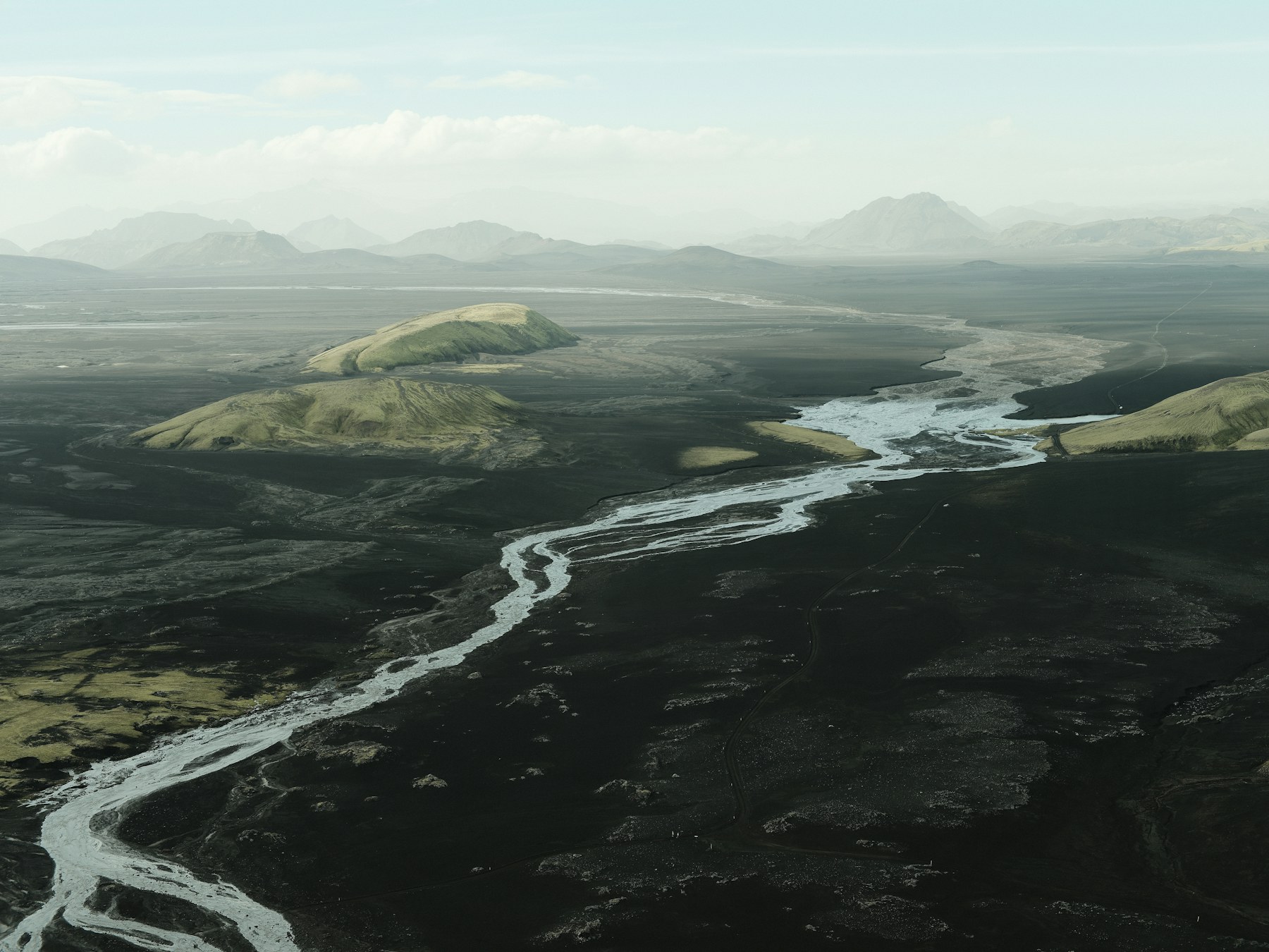 Aerial view of a braided river finding its way through black volcanic terrain